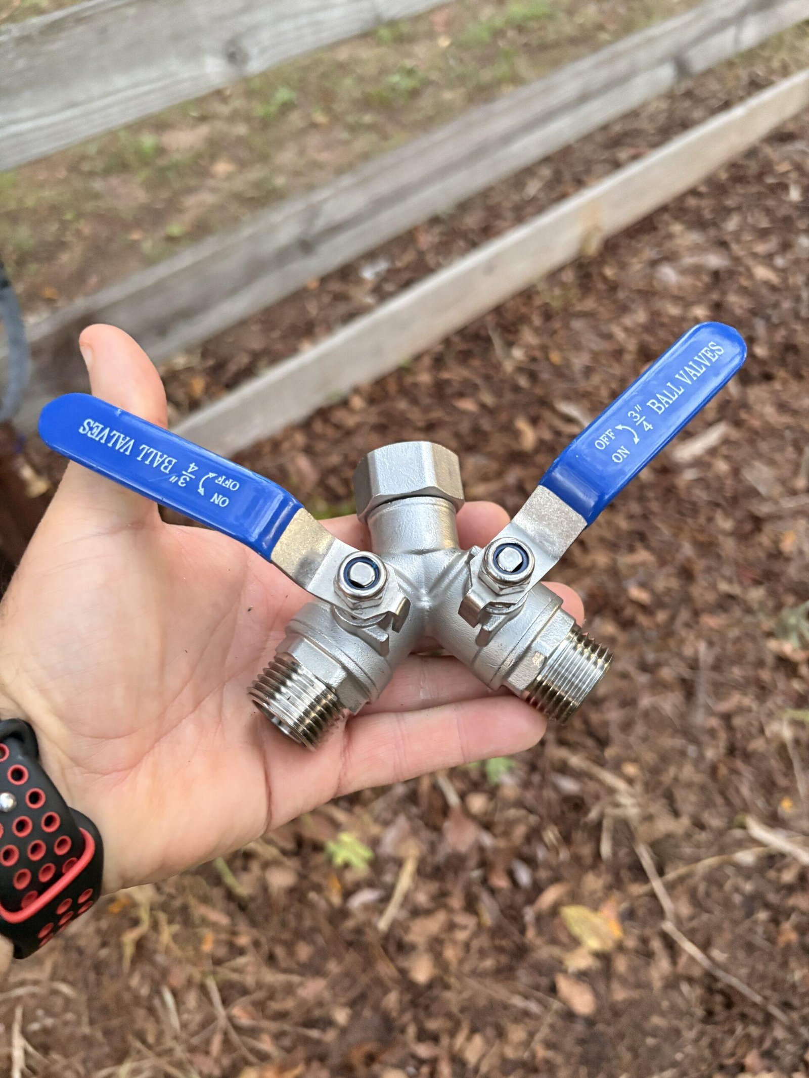 Close-up of a ball valve hose splitter being held in hand before installation on an outdoor water spigot for a drip irrigation system.