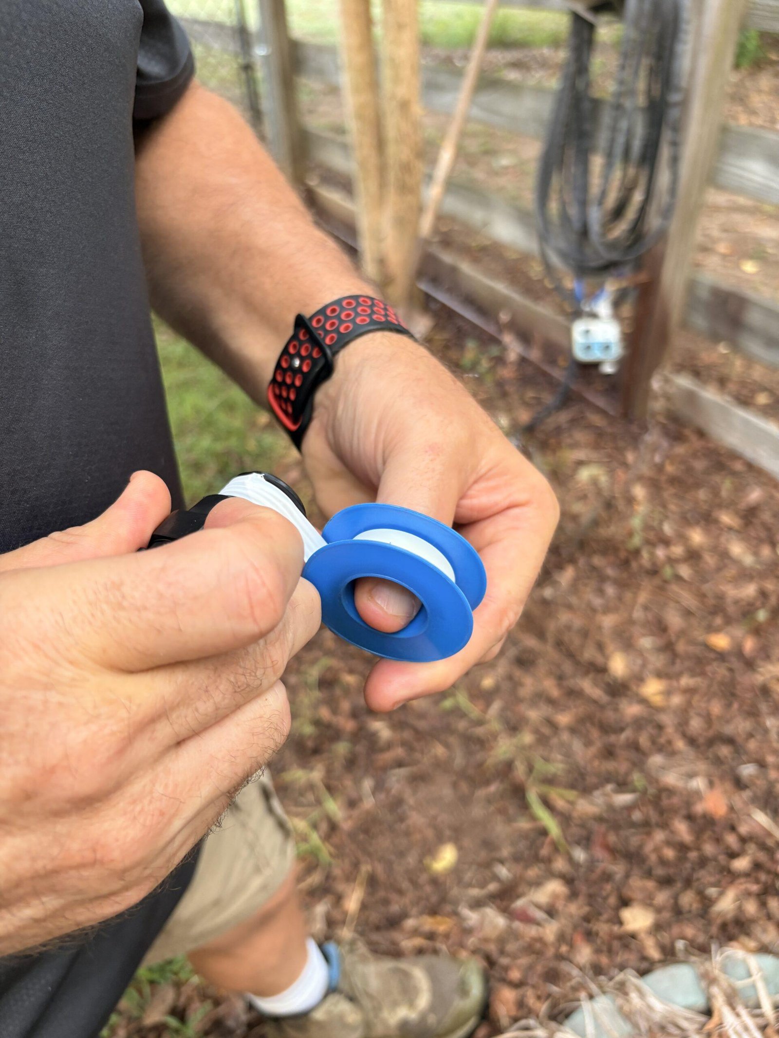 Close-up of hands wrapping Teflon tape around the threaded hose connection before assembling a drip irrigation system.