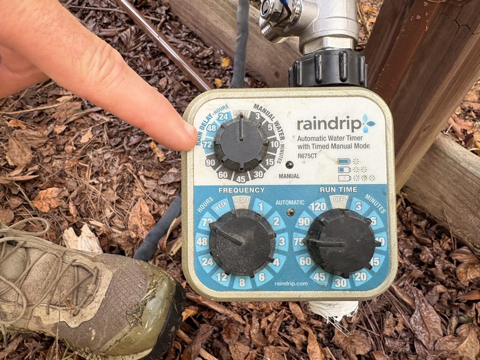 Close-up of a finger pointing to the settings on a drip irrigation water timer used to control the garden watering schedule.