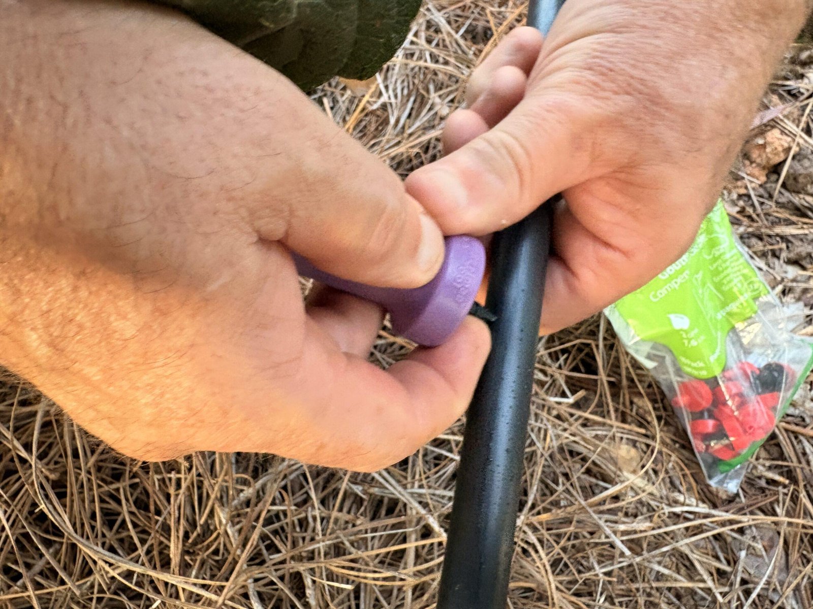 Close-up of hands installing a drip emitter into drip irrigation tubing during garden watering system setup.